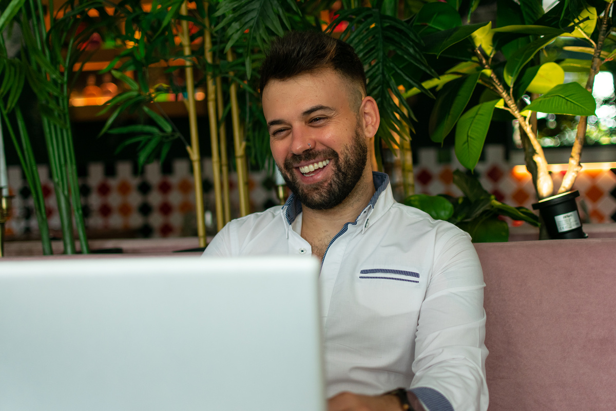 happy man working in kitchen and laughing while looking at blurred laptop